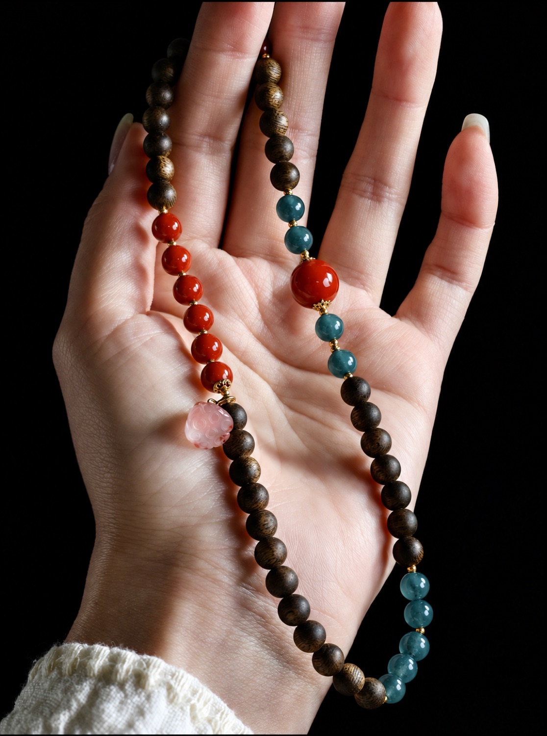 No. 03 相思有寄 hanging from an open hand: vermilion, blue-teal and deep brown beads, a pale pink drop