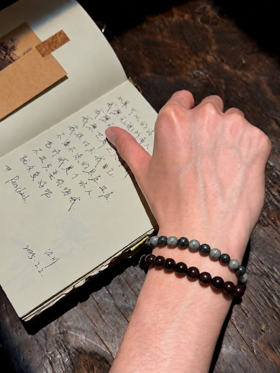 A hand writing in a notebook, two strands of beads on the wrist (No. 04)
