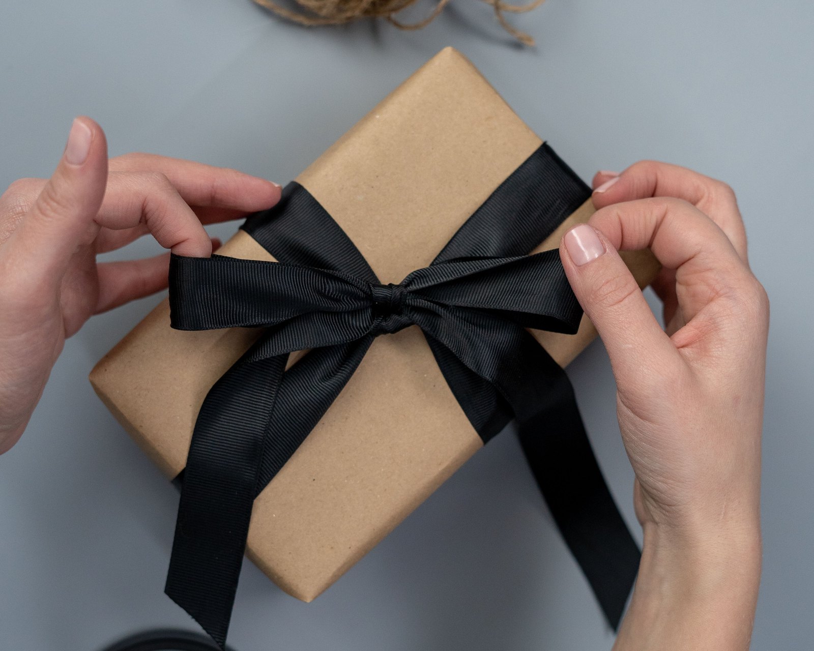 A black ribbon tied around a small box wrapped in plain paper