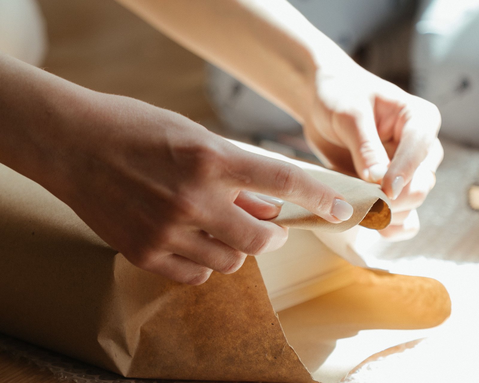 Hands folding plain paper around a gift in window light