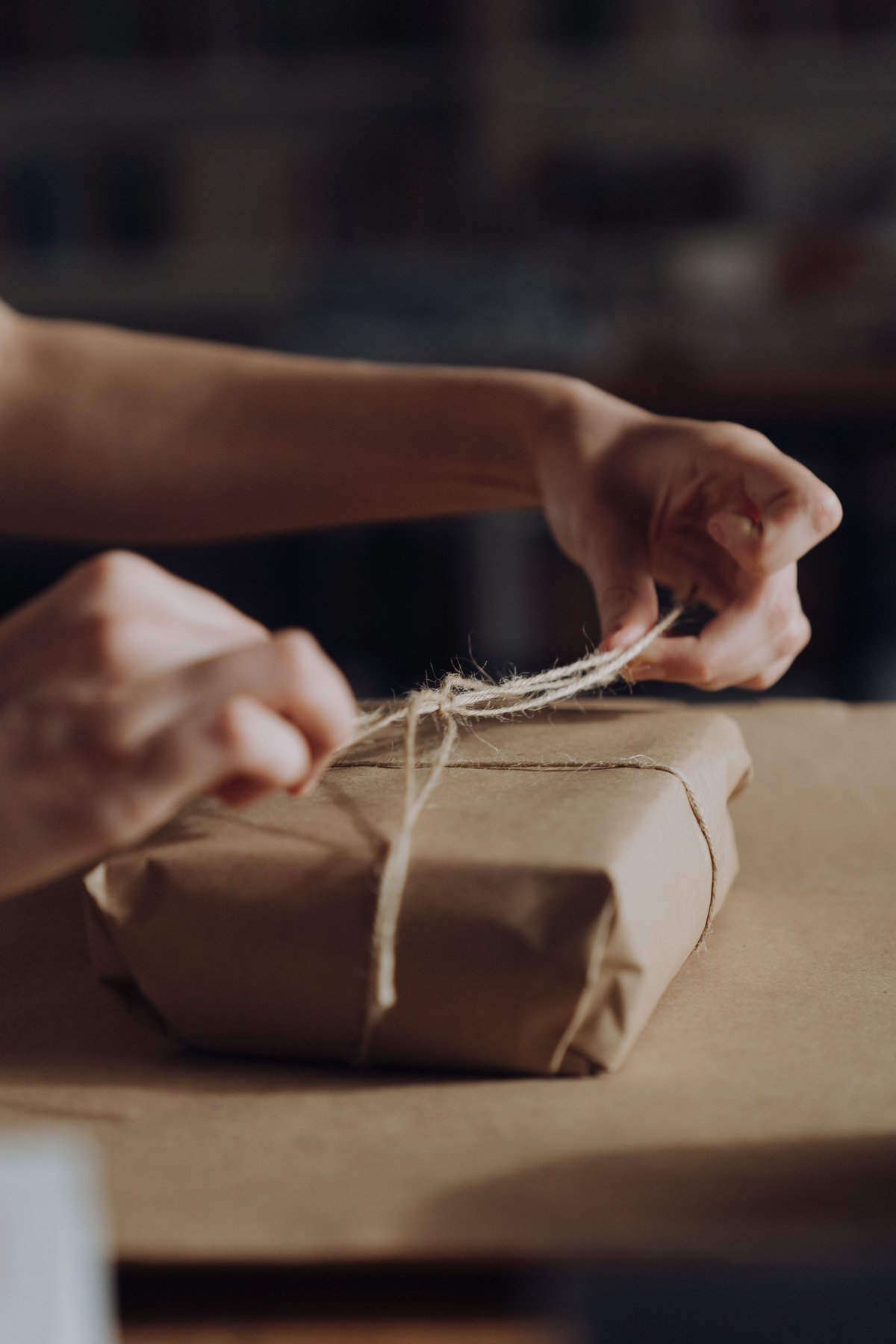 Two hands pull a cord tight around a small parcel wrapped in plain paper
